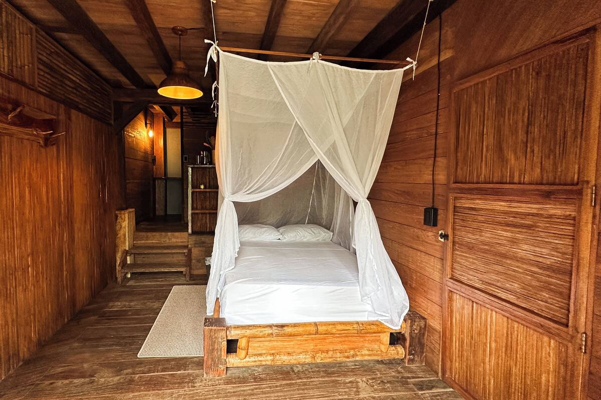 Quarto de madeira com cama de dossel, piso de madeira e luminária pendente.