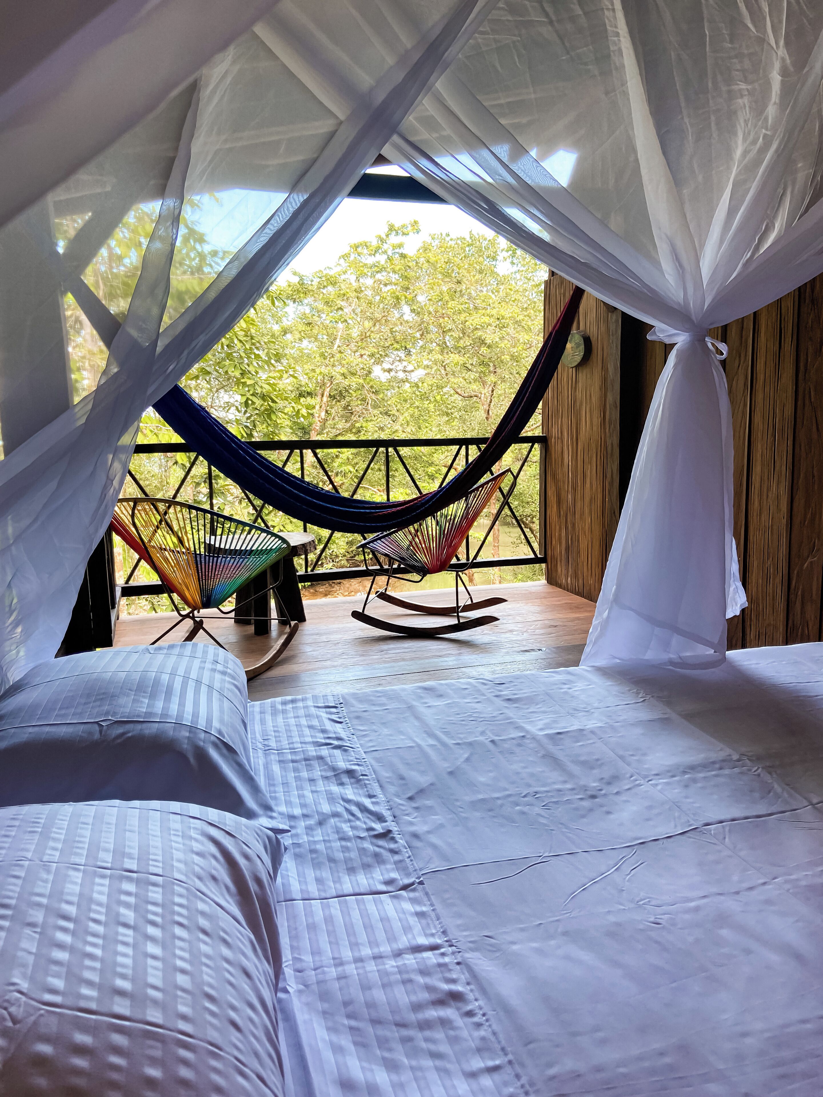 Um quarto com uma cama, uma rede e uma cadeira de balanço.