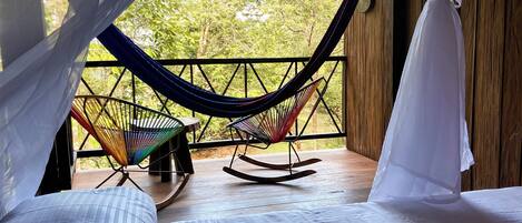 Um quarto com uma cama, uma rede e uma cadeira de balanço.