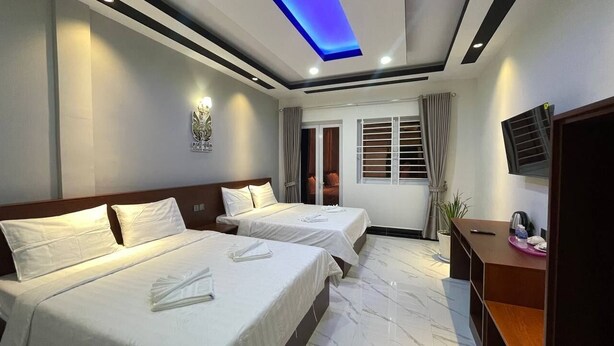 A hotel room with two beds, a TV, a desk, and a ceiling light. - SoursdeiSawadeeBoutique (Kampot)