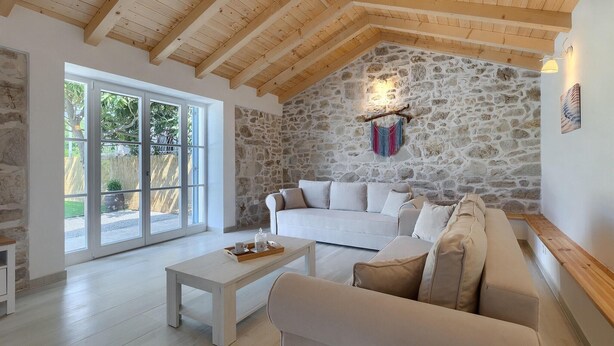 A cozy living room with a stone wall, wooden ceiling beams, a white sofa, and a coffee table.
