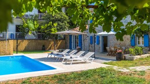 A pool area with lounge chairs and a covered seating area, surrounded by stone walls and vegetation.
