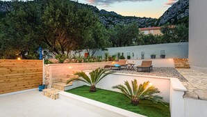 Eine moderne Außenpatio mit einer Steinwand, einem Rasenstück und zwei Lounge-Stühlen.