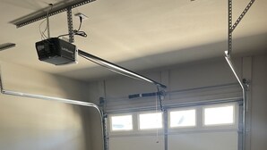 A garage with a ceiling-mounted projector, a garage door with windows, and a concrete floor with stains.