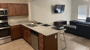 A modern kitchen with granite countertops, wooden cabinets, a built-in dishwasher, and a stainless steel stove.