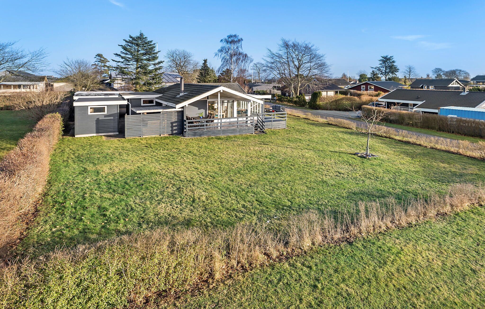 Ett modernt hus med en stor veranda, omgivet av en välskött gräsmatta och andra hus i området.