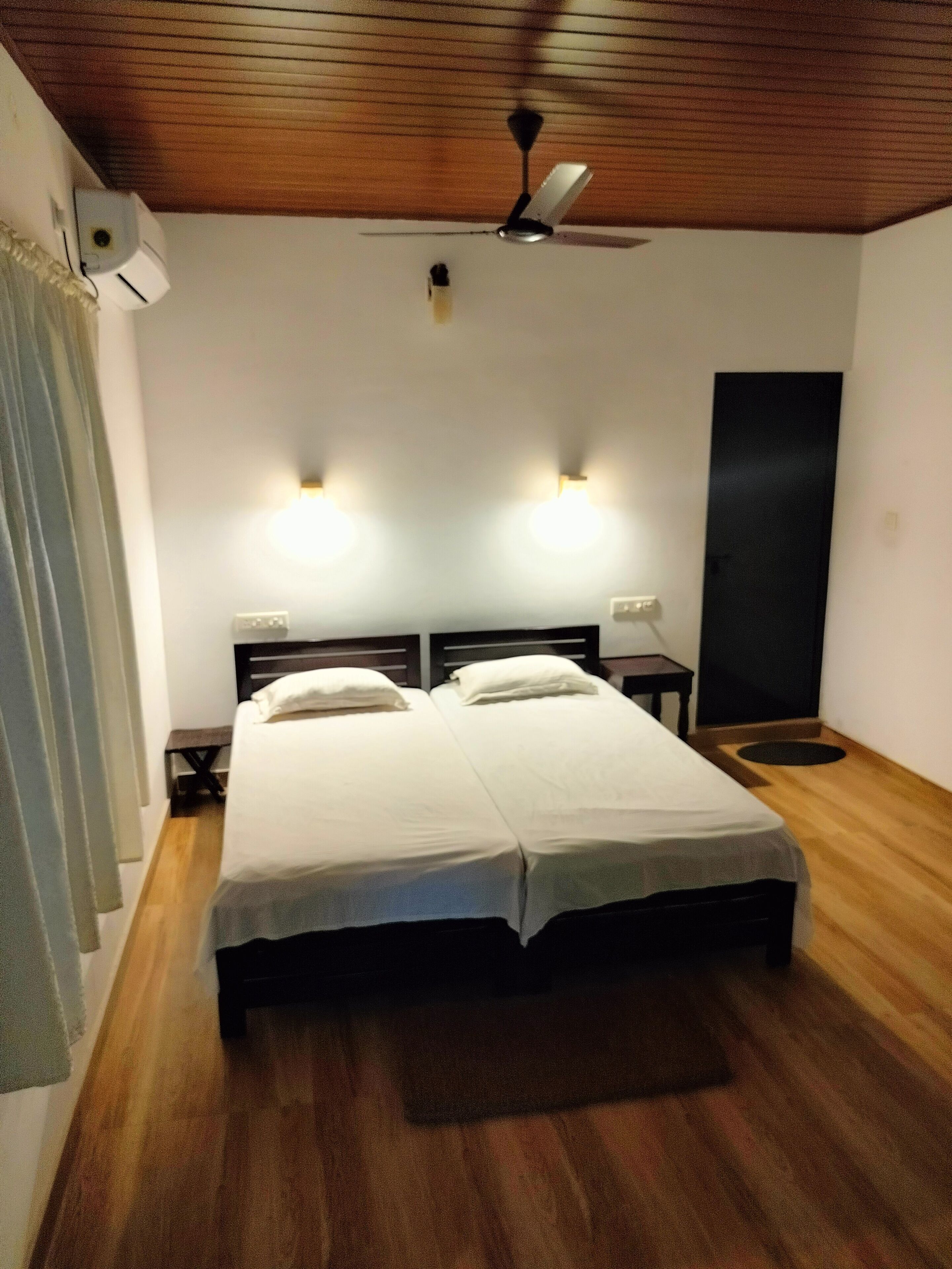 A double bed with white linens in a room with wooden flooring and a ceiling fan.