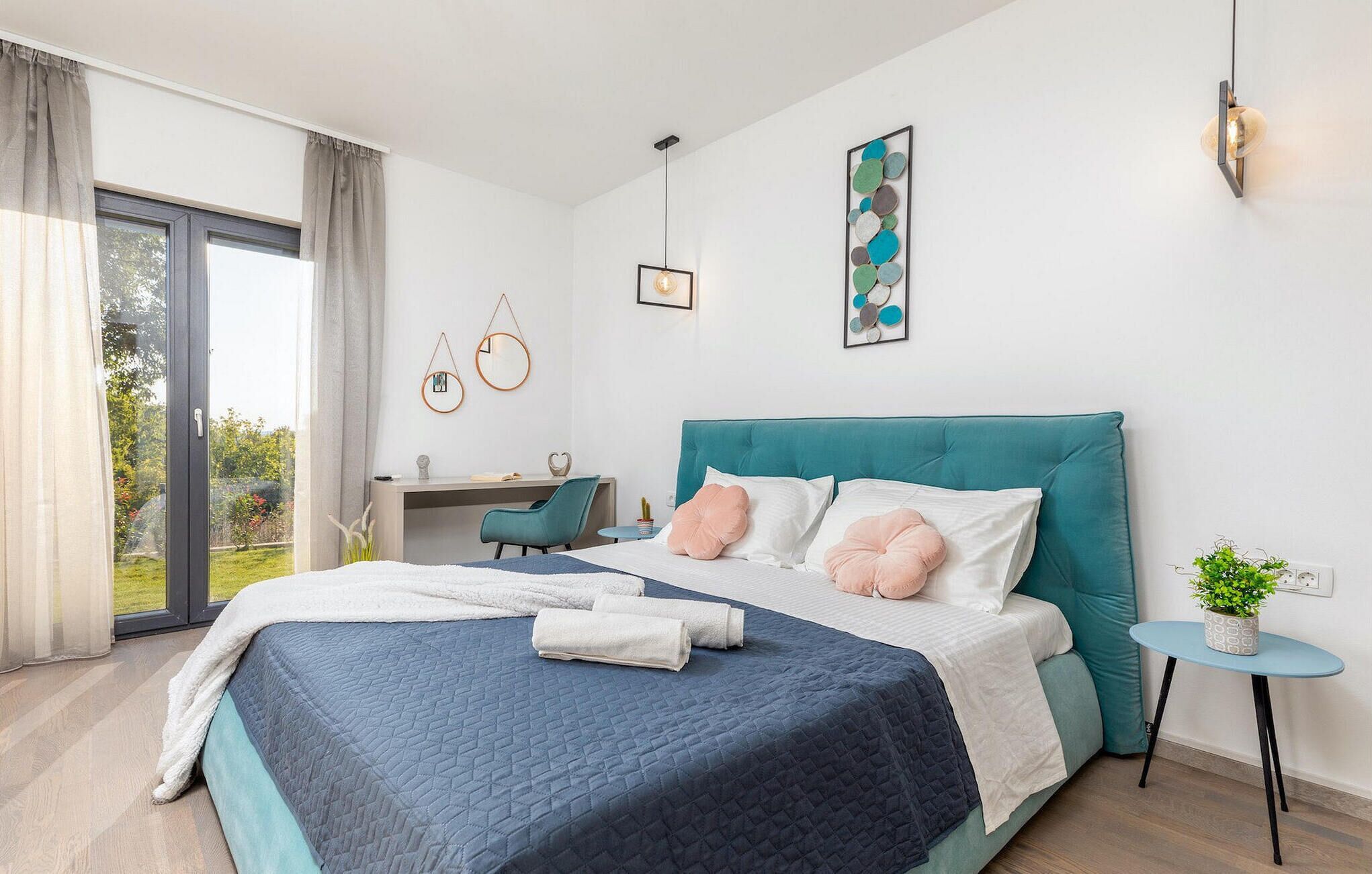 A modern bedroom with a large bed, a desk, and a view of the outdoors.
