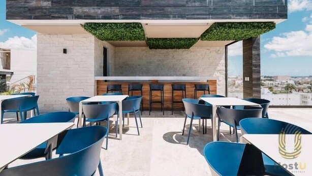 A rooftop bar with blue chairs and tables, a stone wall, and a view of the city. - Stylish Studios Pool Near Beach (Playa del Carmen)