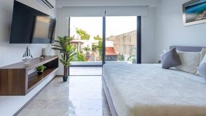 A modern bedroom with a large bed, a TV mounted on the wall, a small plant, and a view of the outside. - Stylish Studios Pool Near Beach (Playa del Carmen)