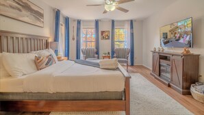 Ein Schlafzimmer mit Bett, Deckenventilator, Fernseher und einem Fenster mit Vorhängen.