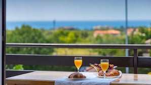 A table with croissants and orange juice glasses, overlooking a scenic view of the sea and greenery.