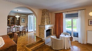 A spacious living area with a fireplace, a dining table set for four, and a view through large windows.