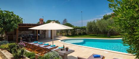 A pool area with lounge chairs, a covered seating area, and a barbecue setup.