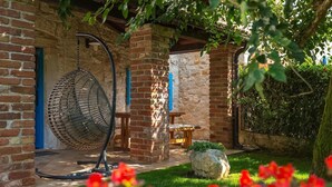 Un patio de ladrillo con una silla colgante, una mesa y un muro de piedra.