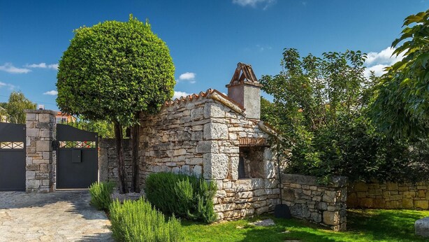 Una casa de piedra con tejado de baldosas, rodeada por un muro de piedra y un jardín bien cuidado.