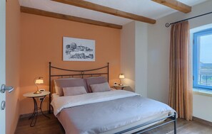 Een slaapkamer met een bed, twee nachtkastjes met lampen, een lijst met een afbeelding aan de muur, en een raam met gordijnen.
