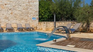 Una piscina con muro de piedra y sillones de descanso.