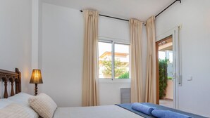 A hotel room with a bed, a lamp, a window with curtains, and a view of the outside. - Cosy apartment for 6 people with WIFI, pool, TV and patio (Torroella De Montgrí)