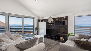 Een moderne woonkamer met een grote televisie, een open haard en een balkon met uitzicht op zee.