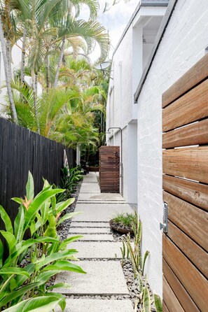 A narrow pathway leading to a wooden door, flanked by a black fence and lush greenery. - 'Villa One' Walk to Noosa Beach & Hastings Street (Noosa)