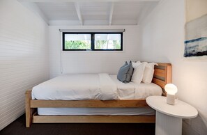 A bedroom with a bed, a bedside table with a lamp, a window with blinds, and a painting on the wall. - 'Villa One' Walk to Noosa Beach & Hastings Street (Noosa)