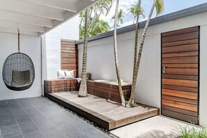 A modern outdoor seating area with a hanging chair, wooden benches, and a wooden door.