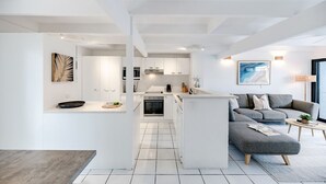 A modern kitchen with white cabinetry, a central island, and a grey sofa in a living area. - 'Villa One' Walk to Noosa Beach & Hastings Street (Noosa)