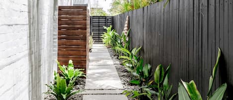 Un étroit sentier bordé d’un mur blanc et d’une clôture en bois, qui mène à un portail.