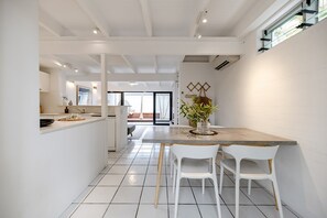 A modern kitchen with white cabinetry, a central island with chairs, and a view to the living area. - 'Villa One' Walk to Noosa Beach & Hastings Street (Noosa)