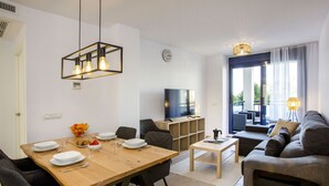 En moderne stue med sofa, sofabord og fjernsyn. Der er et spiseområde med et træbord og stole.