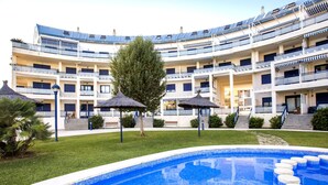 Et hotel med swimmingpool, flere balkoner og en central gårdsplads med træer og parasoller.