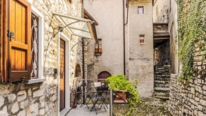 Une ruelle étroite pavée de pierres, avec une table et des chaises, une porte en bois et un pot de fleurs.