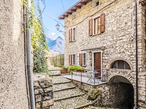 Un edificio de piedra con un pequeño espacio de asientos al aire libre, una escalera que lleva a una puerta y una montaña al fondo.