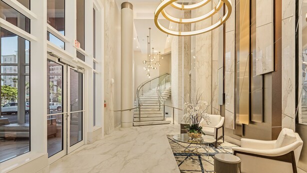 Een moderne hotellobby met een marmeren vloer, een glazen salontafel, een witte bank en een trap naar een andere verdieping.