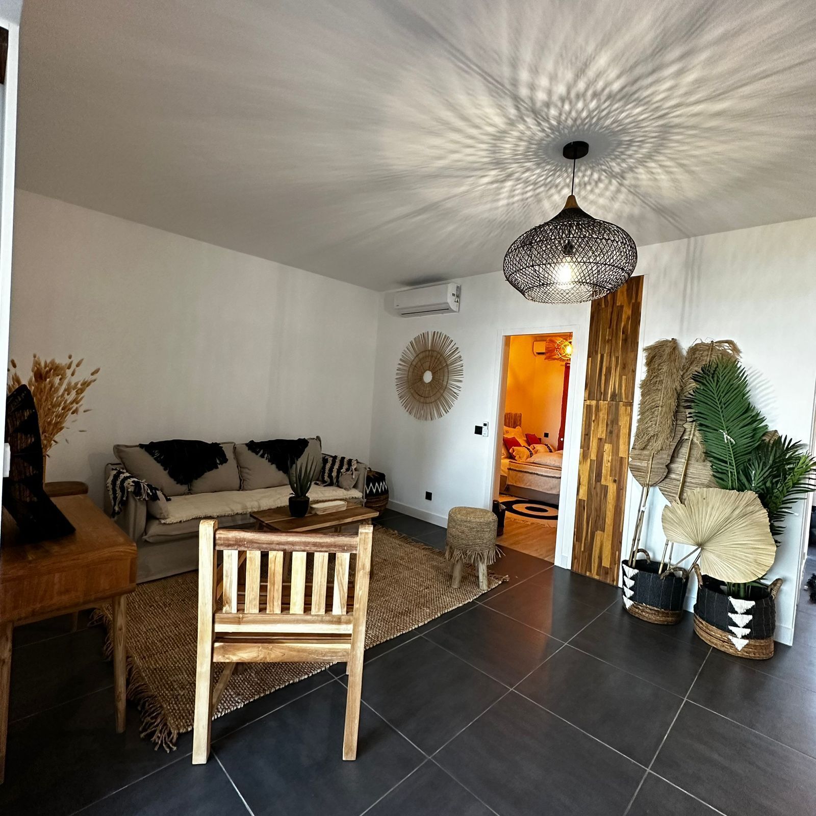 Ett modernt vardagsrum med en soffa, en trästol, en hängande lampa och en dekorativ väggdekoration.