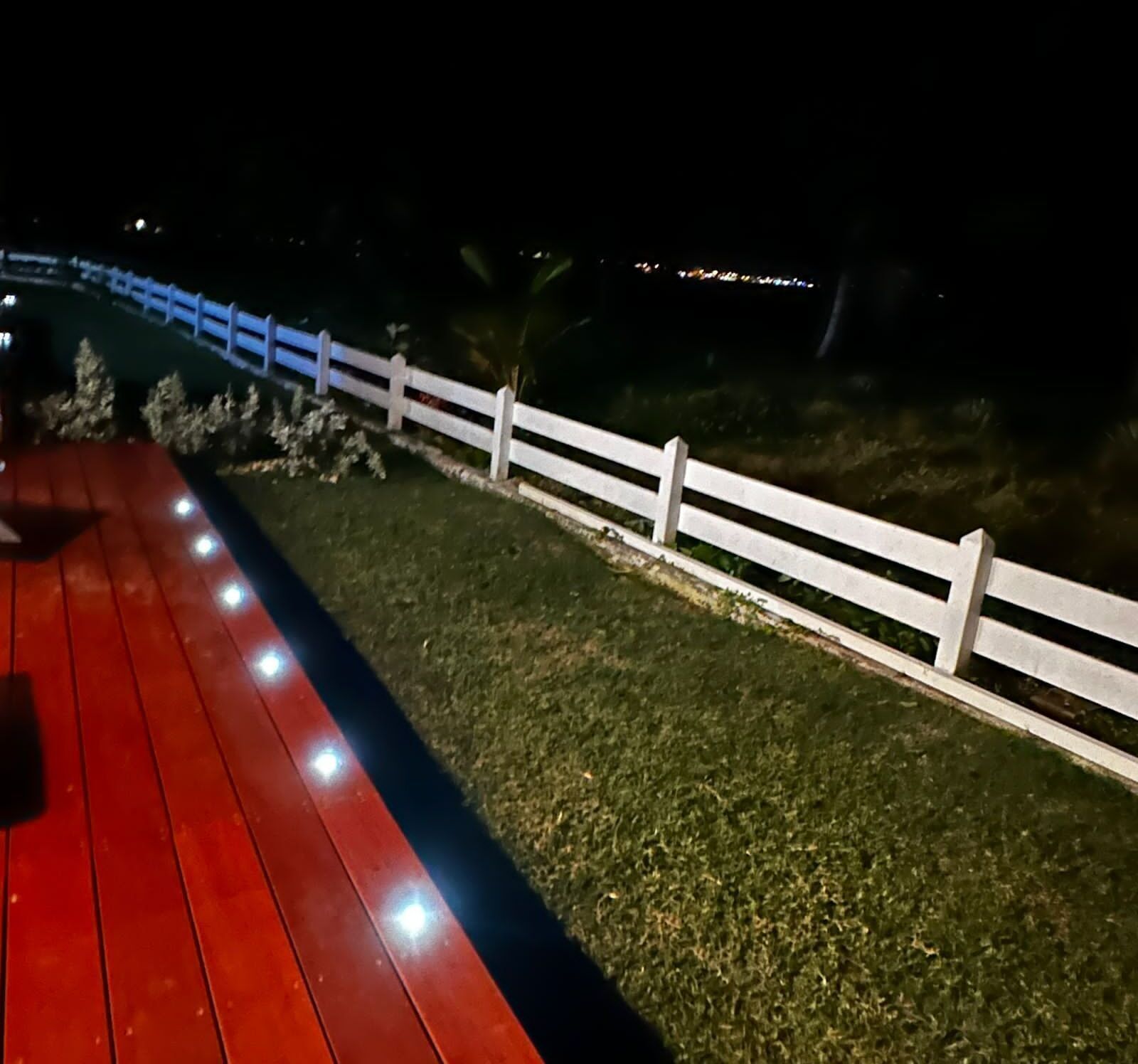 Eine rote Terrasse mit weißem Zaun und Rasen.