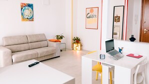 Un salon moderne avec un canapé, une table basse, un bureau avec un ordinateur portable et une petite plante.