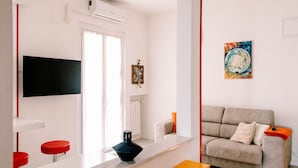 Un salon moderne avec un canapé, un téléviseur à écran plat fixé au mur et un tableau accroché au mur.