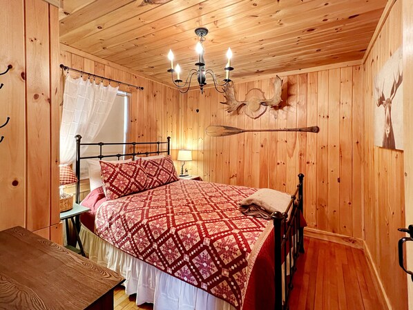 Un dormitorio con paneles de madera, una cama, una araña y una cabeza de ciervo montada en la pared.