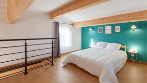 Ein Schlafzimmer mit Bett, einem Fenster mit Vorhängen, einer Wand in Türkis und einem schwarzen Metallgeländer.