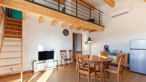 Eine geräumige Küche mit Holzboden, ein Essbereich mit Holzstühlen, eine Treppe und ein Schlafzimmer mit Balkon.