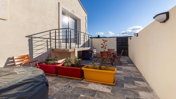 Eine kleine Terrasse im Freien mit einer Holzbank, einem Tisch und Pflanzen in Töpfen.