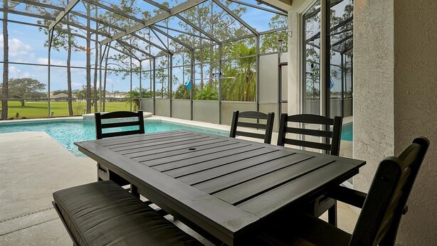 A covered patio with a pool, wooden table, and chairs, overlooking a golf course. - Disney Family Villa w/screened-in patio, pool and spa. Peaceful golf community. (Davenport)