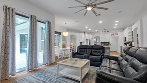 A modern living room with a black leather sofa, a glass coffee table, and a dining area with white chairs. - Disney Family Villa w/screened-in patio, pool and spa. Peaceful golf community. (Davenport)