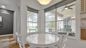 A dining area with a round table and white chairs, large windows with a view of a pool and greenery, and a ceiling fan. - Disney Family Villa w/screened-in patio, pool and spa. Peaceful golf community. (Davenport)