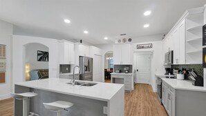 A modern kitchen with white cabinetry, a central island with a sink, and a herringbone tile backsplash. - Disney Family Villa w/screened-in patio, pool and spa. Peaceful golf community. (Davenport)