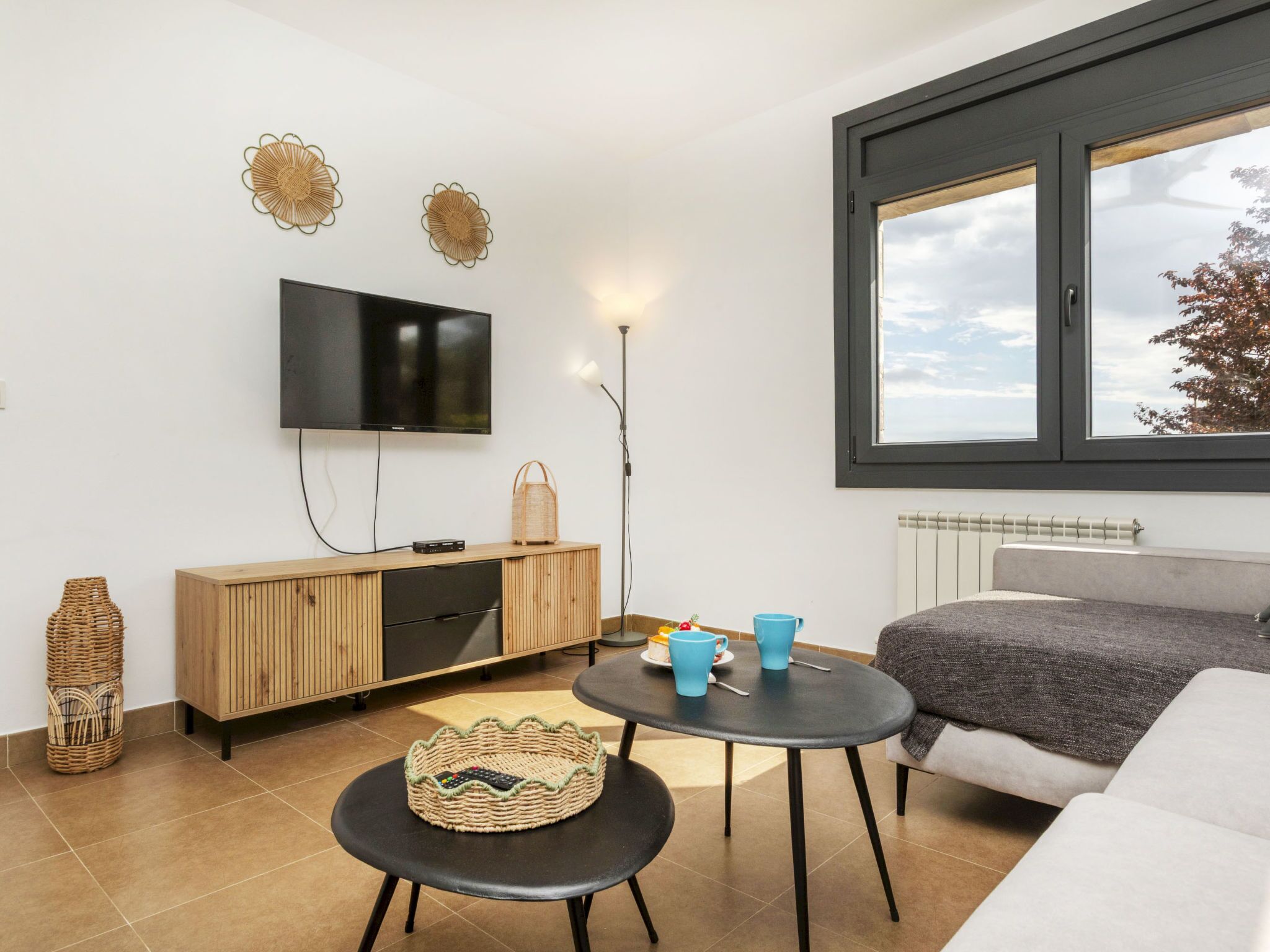 Un salon moderne avec un téléviseur, un meuble en bois, un panier en osier et un canapé.