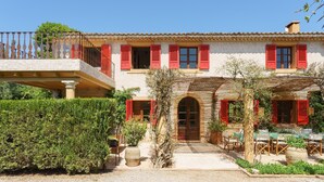 A two-story building with red shutters, a balcony, and a garden with outdoor seating.