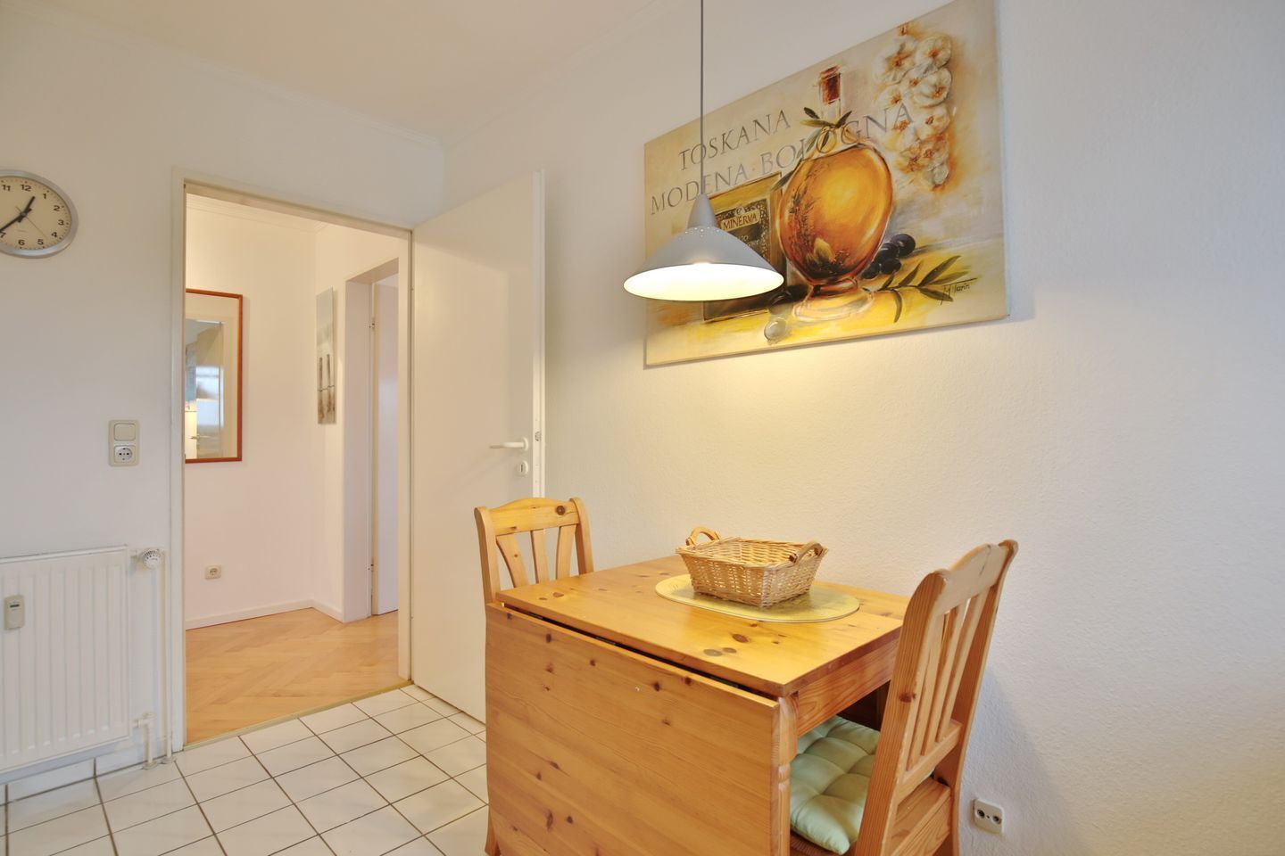Een eetgedeelte met een houten tafel, twee stoelen, een mand en een wandlamp.